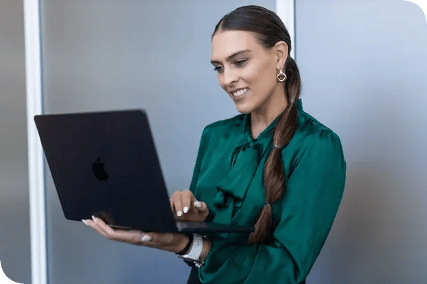 Smiling woman in a green blouse working on a laptop in an office.
