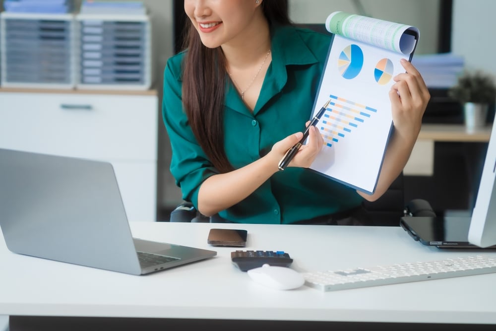 Attractive Asian businesswoman in formal business attire is working at her desk with a laptop and mobile phone, focusing on corporate law, contracts, compliance, and law firm marketing strategies. See less
